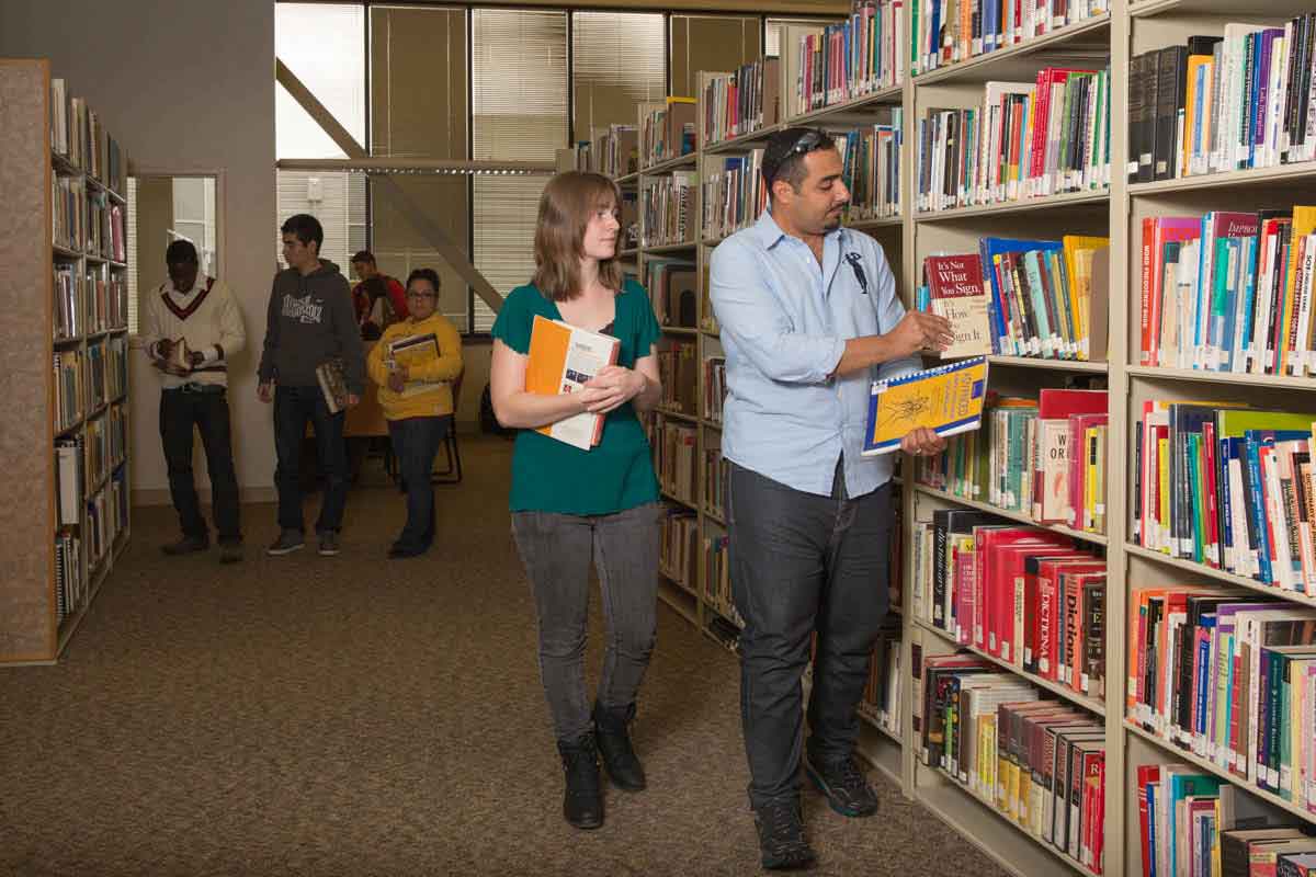 Students standing in the next the stacks of books